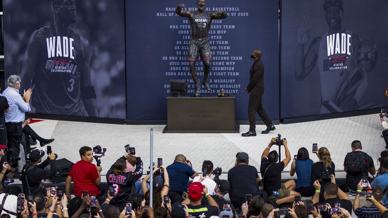 dwyane wade walking in front of his statue in miami as a crowd looks on