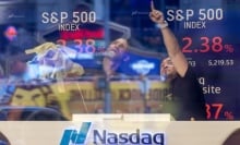 Two men at the NASDAQ stock exchange point at falling numbers on a screen.