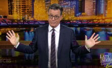 A man stands on a stage with his arms gesturing wide, looking into the camera.