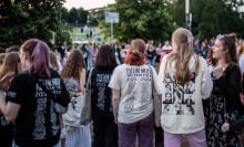 Taylor Swift fans decked out in merch standing in a crowd.