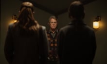 A man stands facing two young women whose backs are to the camera.