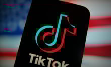 An phone displaying the TikTok logo in front of a blurry American flag.