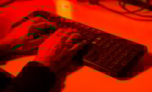 A hand typing on a keyboard bathed in red light.
