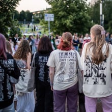 Taylor Swift fans decked out in merch standing in a crowd.