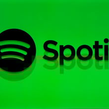 The silhouette of a man in front of a bright green backdrop that reads, "Spotify" with the Spotify logo next to it.