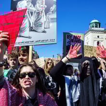A group of pro-Palestinian protesters gather holding flags, signs, and large red triangles.