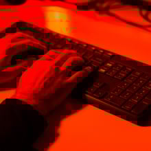 A hand typing on a keyboard bathed in red light.
