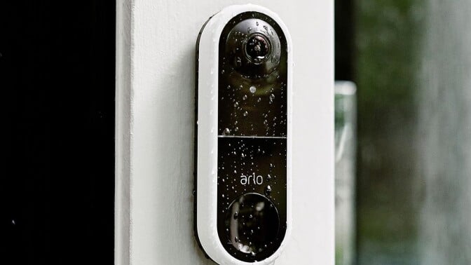 the arlo essential wired video doorbell on the site of a house while its raining