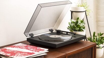 black record player on wooden table next to records in sleeves