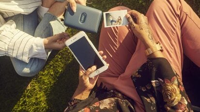 Two people exchanging phone, photo printer, and polaroid