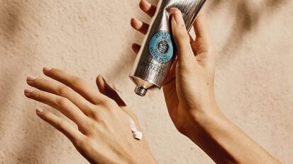 Hand squeezing hand cream from silver tube onto other hand