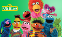 A group of Sesame Street and Plaza Sesamo characters smile to camera.