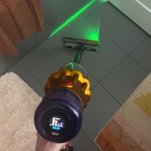 Hand cleaning tile bathroom floor with Dyson V12 Detect Slim vacuum and green laser highlighting debris on floor