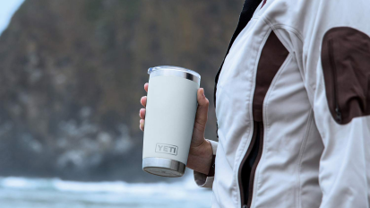 hand holding white tumbler in front of ocean view