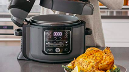 hand lifting lid of multicooker with roast poultry in front of it