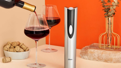 Silver and black wine opener next to two glasses of wine, one with wine being poured into it