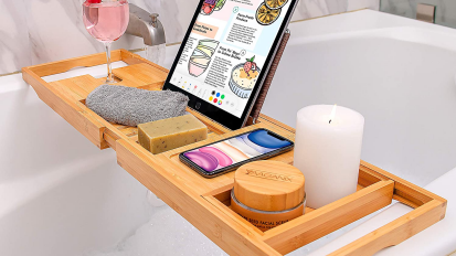 wooden tray suspended over bathtub with tablet, phone, drink, towel, soap, and candle